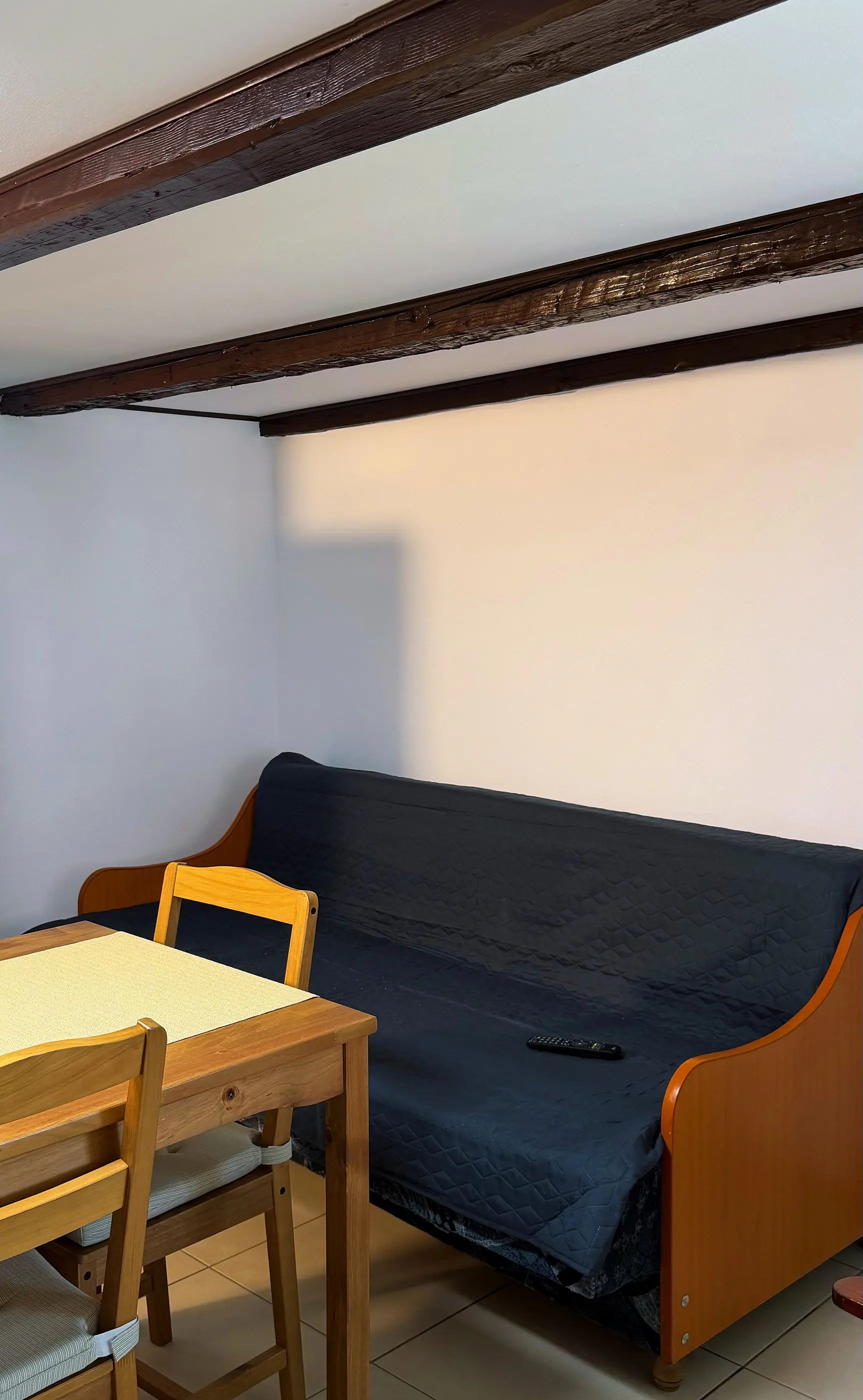 A sofa under the wooden beams, next to the kitchen table