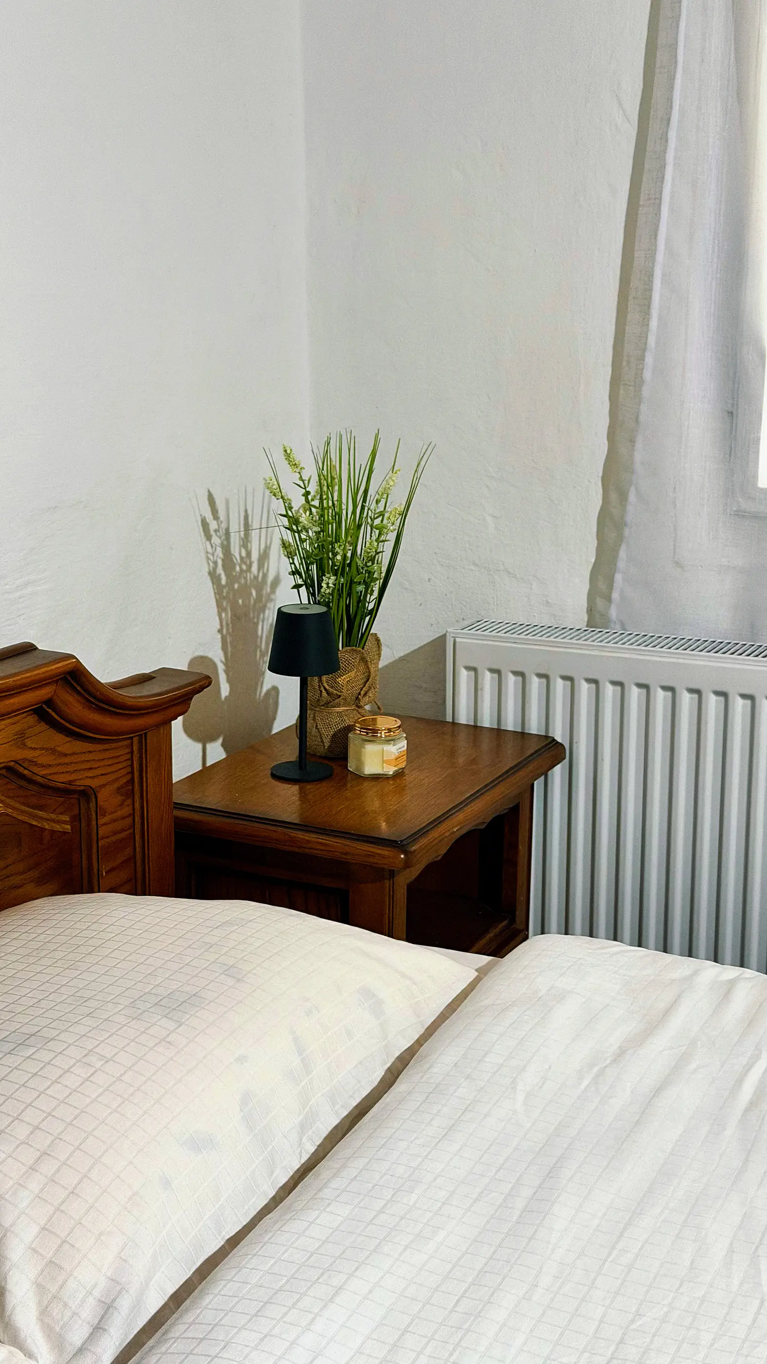 A wooden bedside table with a lamp and a plant, by the window