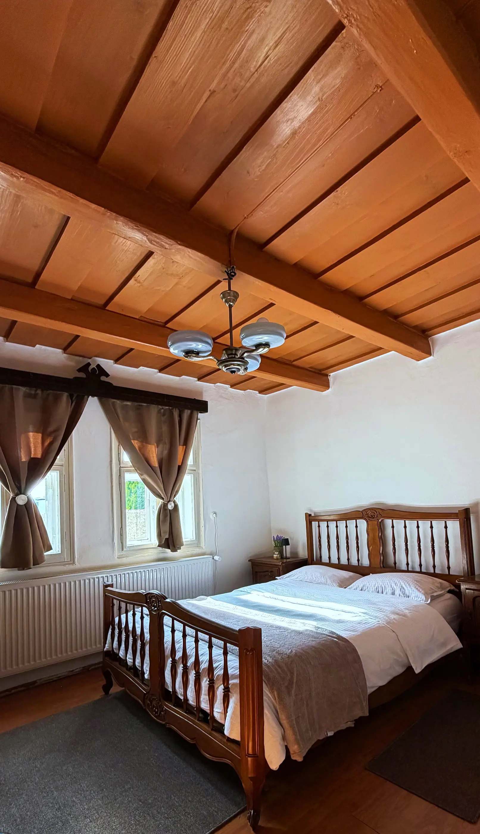 Bedroom with a wooden ceiling, a wooden double bed and curtains